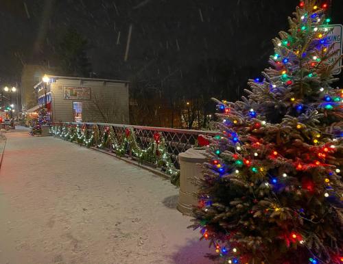 A snowy night scene featuring a decorated tree and festive lights along a bridge, with holiday decorations visible.