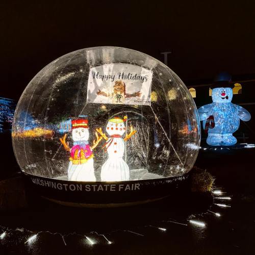 A festive snow globe display at the Washington State Fair featuring snowmen and a "Happy Holidays" sign.
