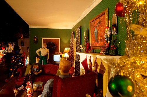 A cozy holiday scene with mannequins, a decorated Christmas tree, stockings, and festive decor in a warmly lit room.