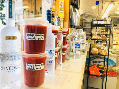 A display of various vodka bottles and containers of Bloody Mary mix in a store, with labels on the mixes.