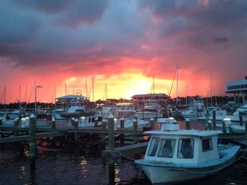 Sunset over a marina with boats docked, vibrant orange and pink skies reflecting on the water.