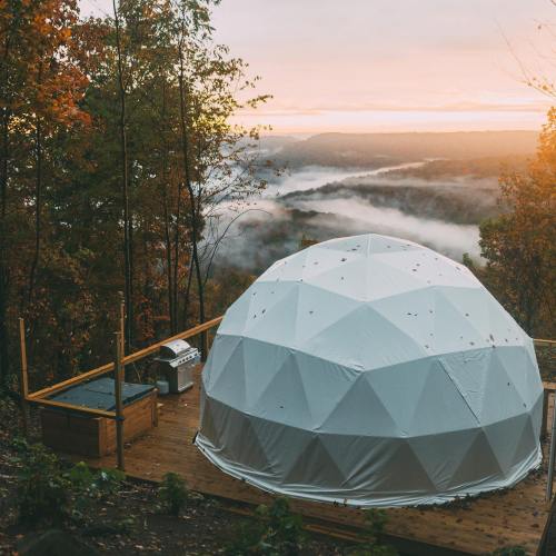 A geodesic dome on a wooden deck overlooking a misty valley and forest during sunset.