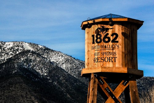 Wooden water tower with "1862 David Walley's Hot Springs Resort" sign, set against a backdrop of snow-capped mountains.