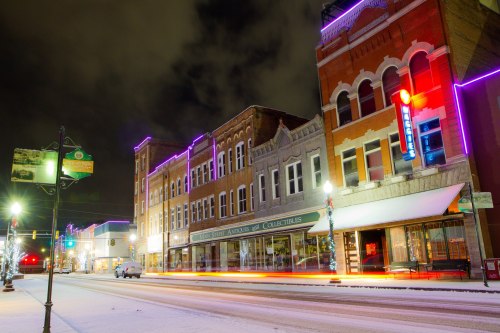A snowy street scene at night, featuring historic buildings adorned with colorful lights.