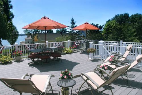 A sunny deck with lounge chairs, a table under an umbrella, and a view of trees and water in the background.