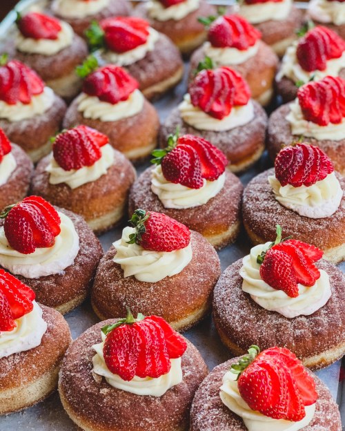 A close-up of freshly baked donuts topped with whipped cream and fresh strawberries, arranged neatly on a tray.