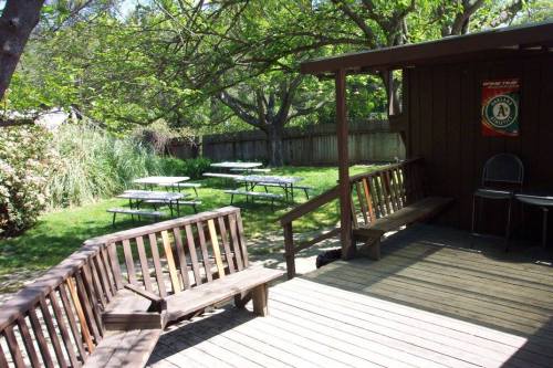 A wooden deck with benches overlooks a grassy area with picnic tables and trees in a sunny outdoor setting.