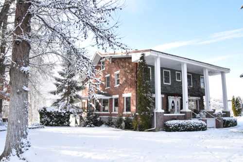 A large brick house with white columns surrounded by snow-covered trees and a winter landscape.