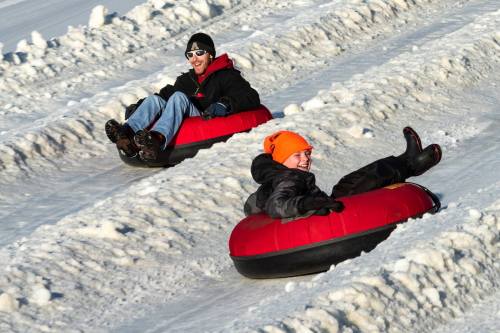 Two people in red snow tubes sliding down a snowy hill, enjoying a winter day.