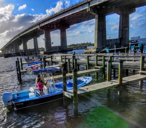 A woman prepares to board a boat at a dock under a bridge, with an American flag displayed nearby.