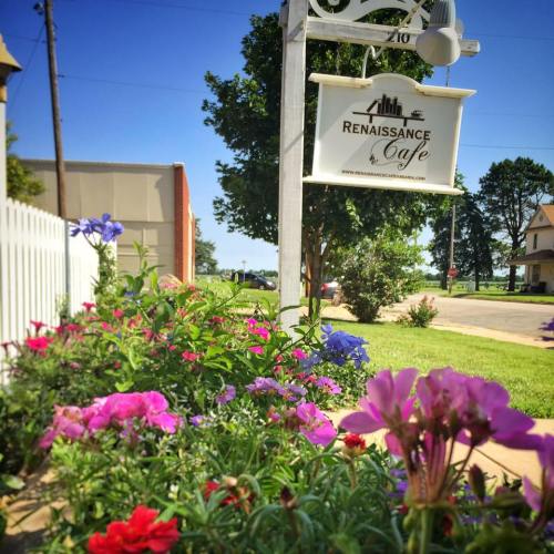 A colorful flower bed in front of a sign for Renaissance Cafe, with trees and buildings in the background.