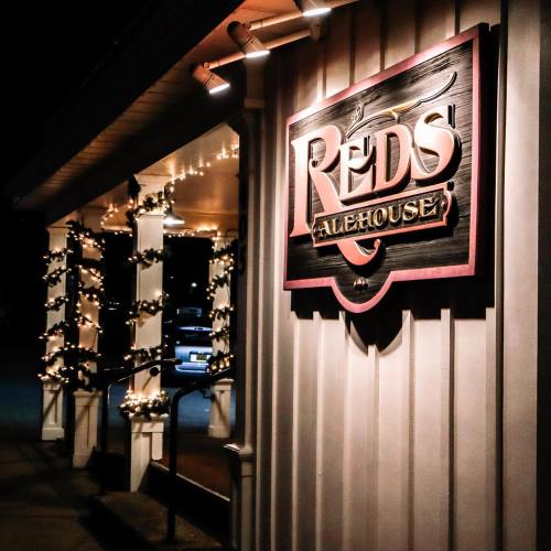 A warmly lit entrance to Reds Alehouse, featuring festive lights and a prominent sign.