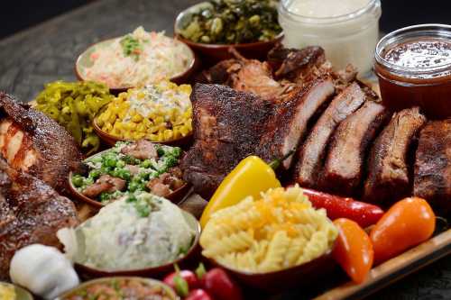 A vibrant spread of barbecue meats, sides, and sauces, featuring brisket, coleslaw, corn, and colorful peppers.