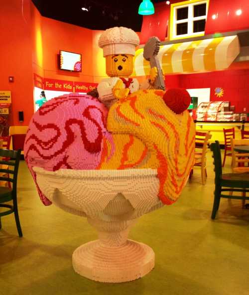 A colorful ice cream sundae sculpture made of building blocks, featuring a chef figure on top, in a vibrant restaurant setting.