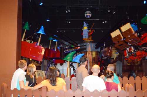 A group of people watches a whimsical display featuring colorful hats and a wizard figure in a playful setting.