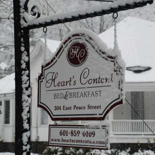 Sign for Heart's Content Bed & Breakfast, covered in snow, with a white house in the background.