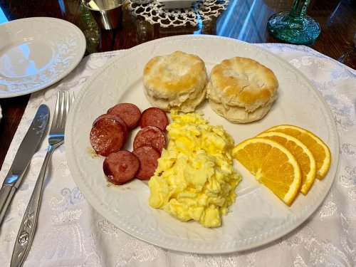 A plate with two biscuits, scrambled eggs, sliced sausage, and orange slices, set on a table with utensils.