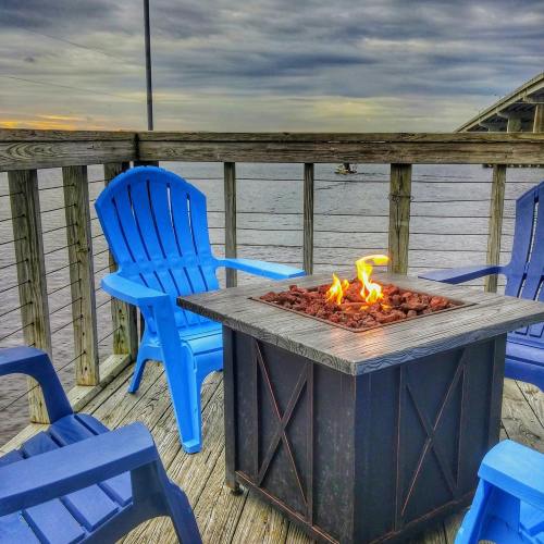 A cozy outdoor seating area with blue chairs around a fire pit, overlooking a calm body of water under a cloudy sky.