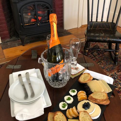 A cozy setting with a bottle of champagne in an ice bucket, plates, and a platter of cheese, crackers, and fruit.