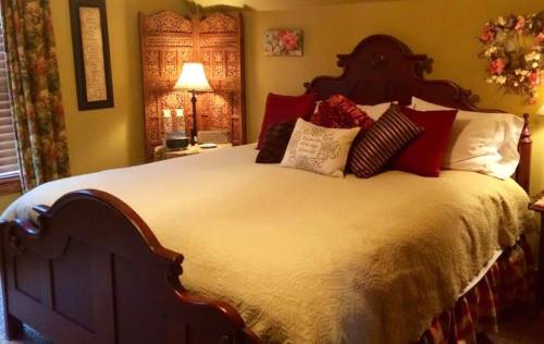 Cozy bedroom featuring a large bed with decorative pillows, a lamp, and a wooden screen in a warm, inviting color scheme.