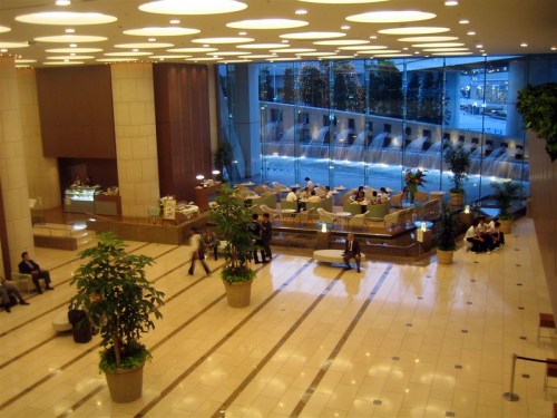 A spacious hotel lobby with modern decor, seating areas, and large windows overlooking a water feature.