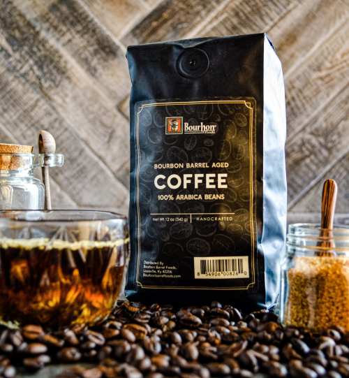 A bag of bourbon barrel aged coffee sits on coffee beans, with a jar of coffee and sugar in the background.
