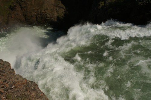 Raging water cascades over rocky cliffs, creating frothy waves in a natural setting.