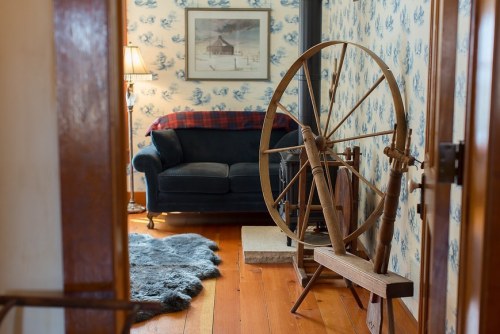 Cozy interior with a spinning wheel, a dark sofa, and floral wallpaper, creating a warm, inviting atmosphere.