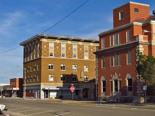 Historic buildings line a quiet street, featuring a mix of brick and ornate architecture under a clear blue sky.