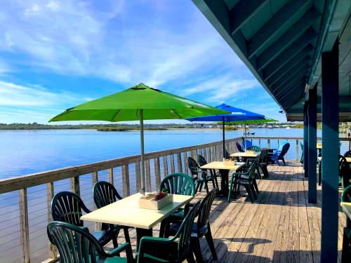 Outdoor dining area with green and blue umbrellas overlooking a calm waterway under a clear blue sky.