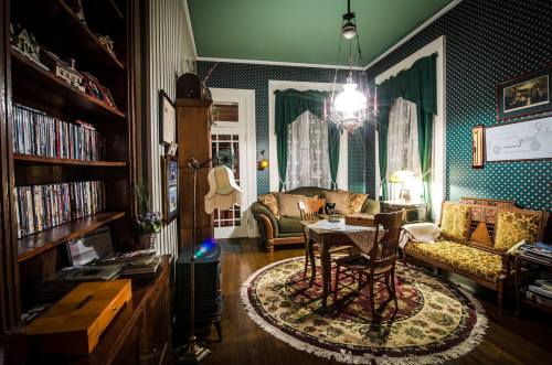 Cozy living room with patterned walls, vintage furniture, a round table, and a bookshelf filled with CDs.