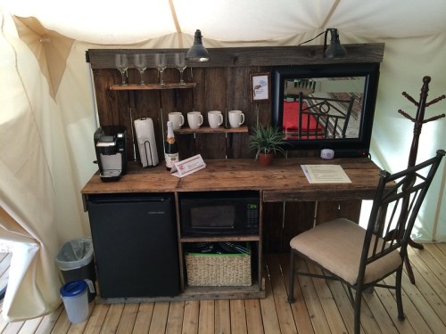 Cozy wooden desk setup with a coffee maker, microwave, and decorative items in a tent-like space.