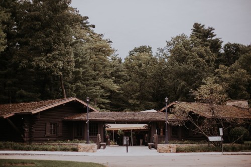 A rustic wooden lodge surrounded by trees, featuring a welcoming entrance and outdoor seating.