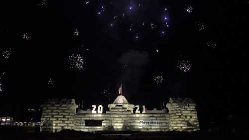 Fireworks illuminate a night sky above a large ice sculpture displaying "2021" and a dome structure.