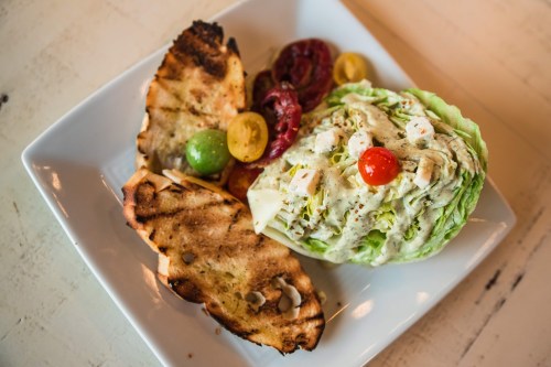 A plate with grilled bread, a wedge salad topped with cherry tomatoes, and mixed vegetables.