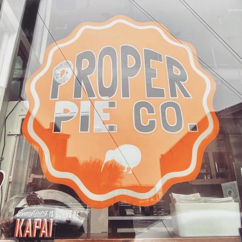 Sign for Proper Pie Co. featuring bold orange text and a white silhouette of a pie, with the phrase "Everything is Gonna Be Kapai."