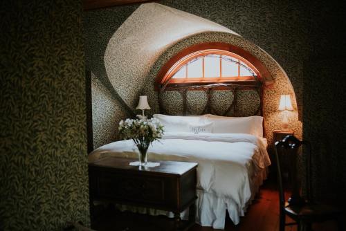 Cozy bedroom with a curved wall, large window, floral wallpaper, and a bed adorned with white linens and a vase of flowers.