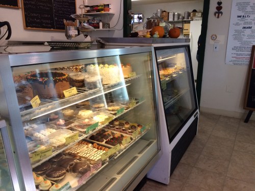 Display case filled with various desserts, including cakes, cupcakes, and pastries, in a cozy bakery setting.