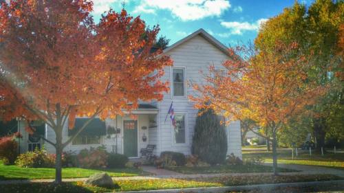 A charming white house surrounded by vibrant autumn trees with orange and yellow leaves under a bright blue sky.