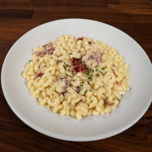 A plate of creamy macaroni and cheese topped with herbs and bits of bacon on a wooden table.
