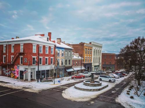 A snowy street scene featuring historic buildings, a fountain, and parked cars in a quaint town.