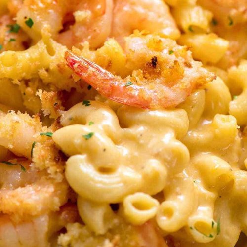 Close-up of creamy macaroni and cheese topped with shrimp and breadcrumbs, garnished with parsley.