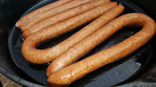 Cooked sausages arranged in a frying pan, sizzling in oil.