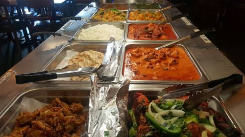 A buffet spread featuring various dishes, including rice, naan, and several curries in metal trays.