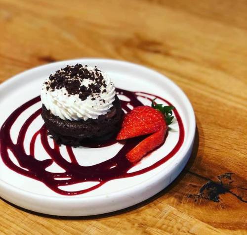 A chocolate dessert topped with whipped cream and chocolate crumbs, served with a strawberry and berry sauce on a white plate.