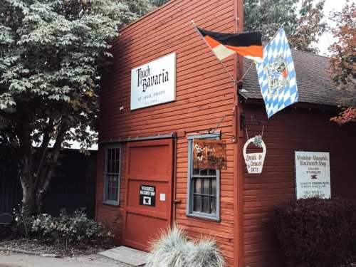 A red wooden building with signs for "Touch of Bavaria" and flags, surrounded by trees and greenery.