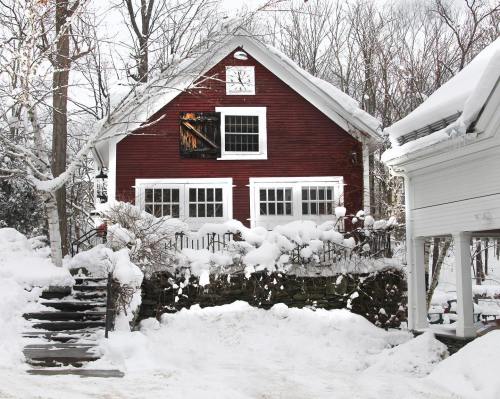 A red house with white trim surrounded by snow, featuring a clock and a window with a partially open shutter.