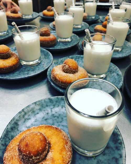 Plates with donuts and glasses of milk, each with a straw, arranged on a table.