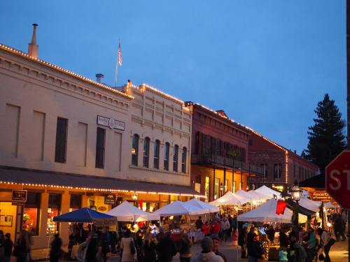 A lively street scene at dusk with people, tents, and buildings adorned with lights.
