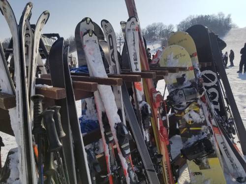 A rack of skis and snowboards on a snowy slope, with people skiing in the background.